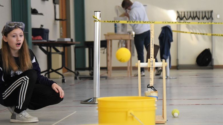 A female student watches a rubber ball fly toward a bucket at the Science Olympiad at Penn State Behrend.