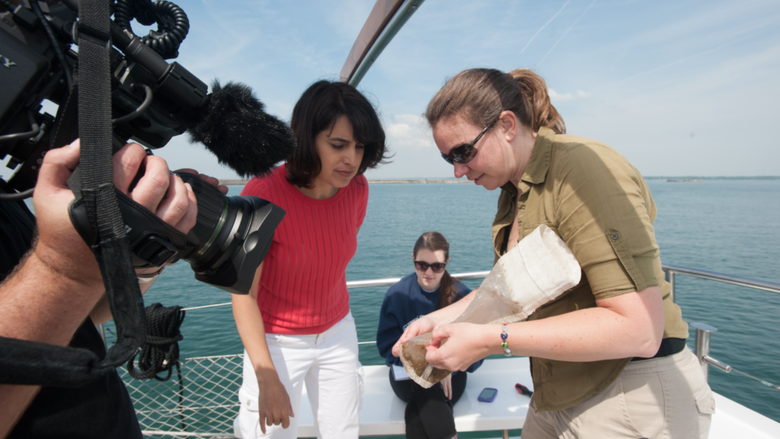 Scientist on boat shows microplastic sample to film crew