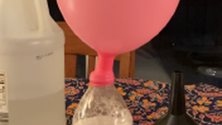 Balloon inflating over lid of water bottle filled with vinegar and baking soda