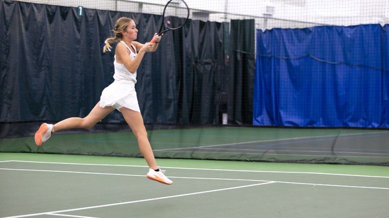 A Penn State Behrend tennis player jumps while hitting the ball.