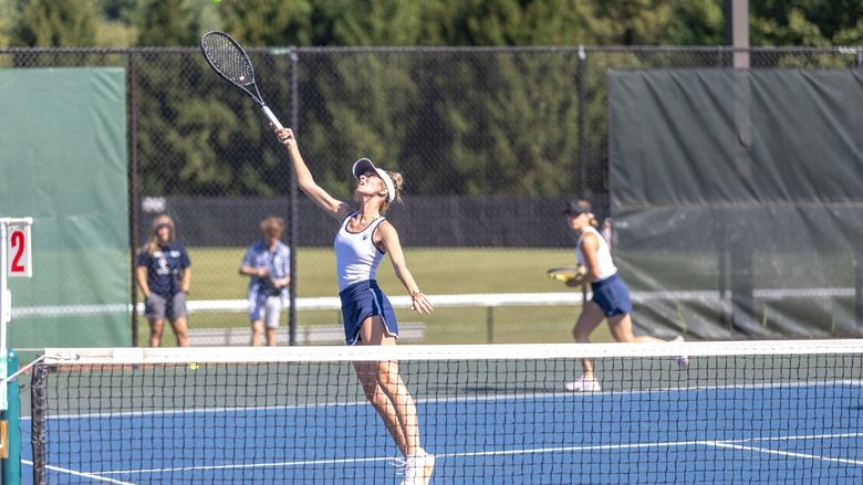 A member of the Penn State Behrend women's tennis team reaches up to hit a ball.