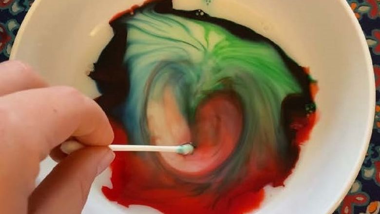 Bowl with milk and food coloring, with a cotton swab coated in dish soap to create a tie-dye milk experiment.