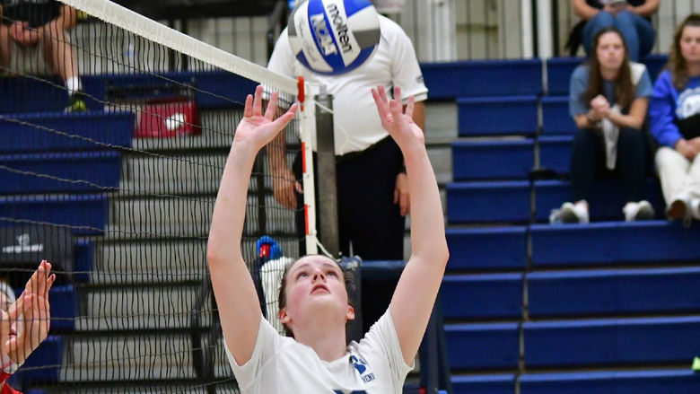 A Penn State Behrend female volleyball player sets the ball near the net.