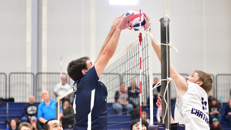Two male volleyball players jump while facing each other at the net.
