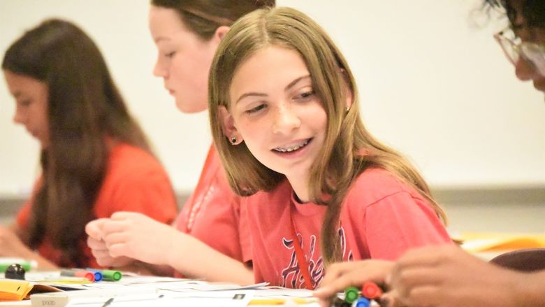 A middle-schooler looks to her side and smiles as a classmate works on a drawing project.