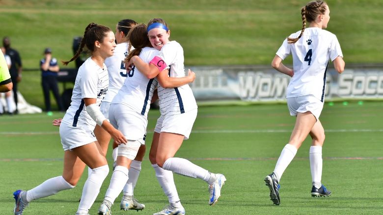 Members of the Penn State Behrend women's soccer team hug and celebrate after scoring a goal.