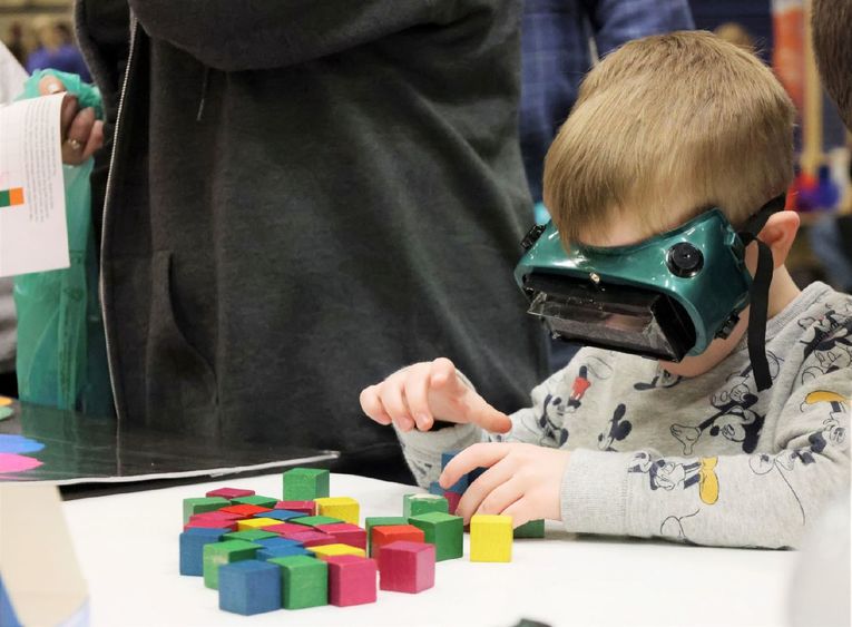 A boy stacks blocks while wearing VR goggles at the Penn State Behrend STEAM fair.