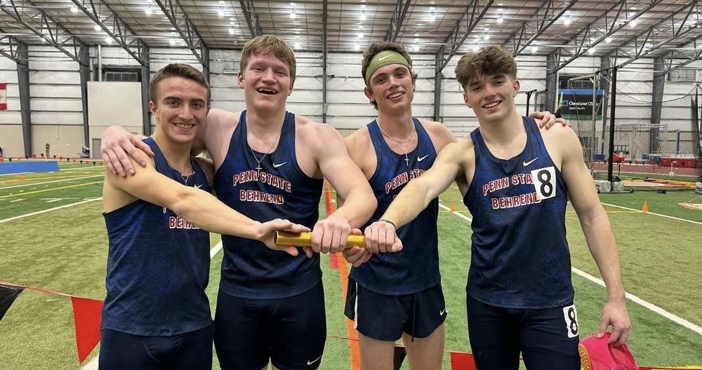 Four Penn State Behrend runners pose while holding a track baton.