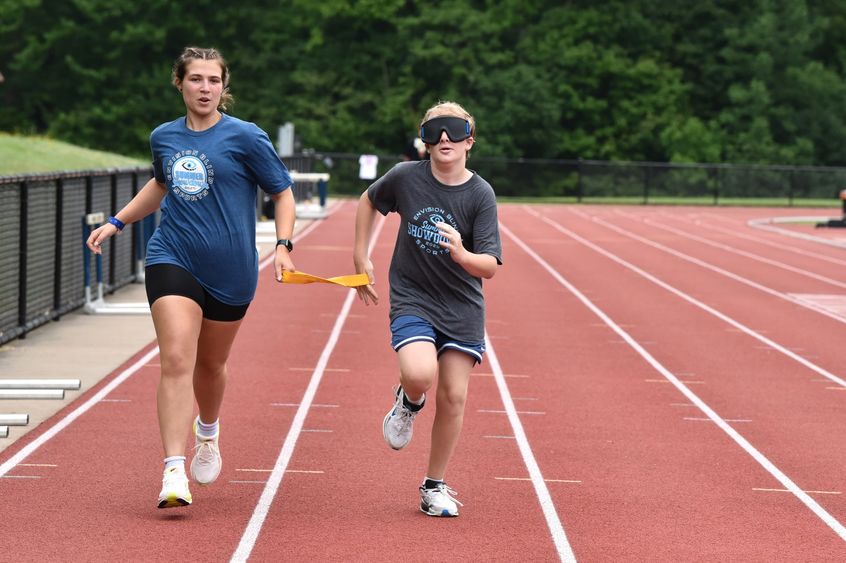 A vision-impaired athlete runs with a guide while holding a tether.