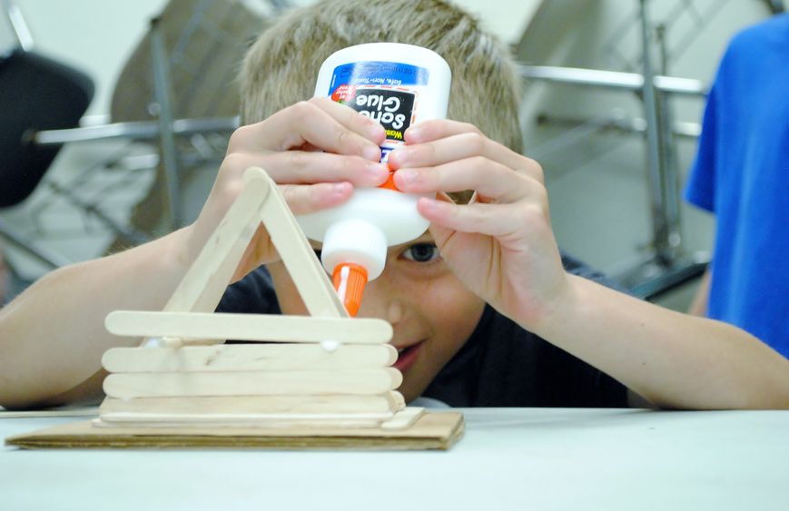 A student builds a pyramid with craft sticks and glue.