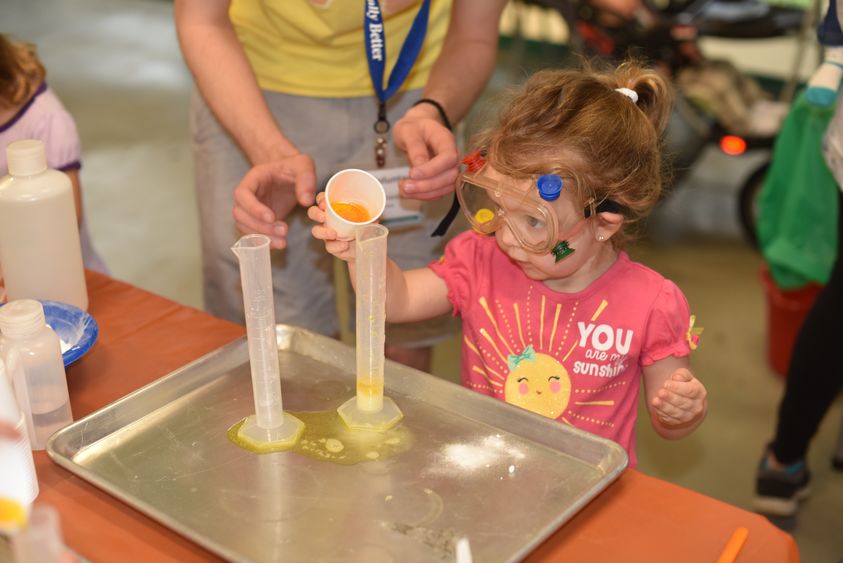 Young preschool-aged girl pours fluid into a beaker.