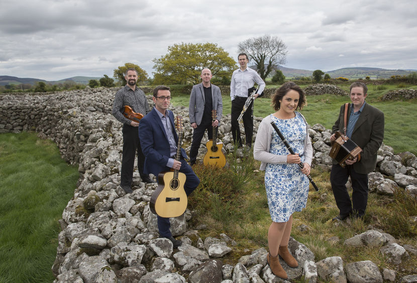 The musicians in the band Danu pose on rocks in a country field.