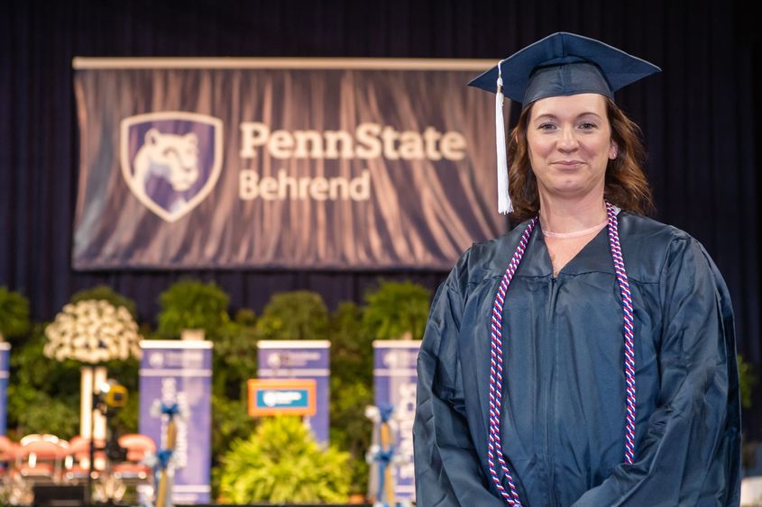 A Penn State Behrend graduate poses on the commencement stage.