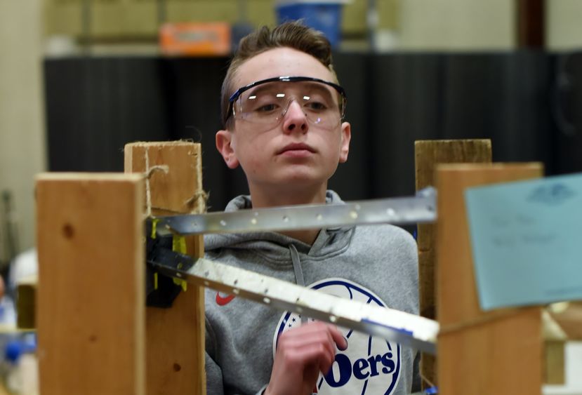 A middle-school student watches a marble roll down a constructed track