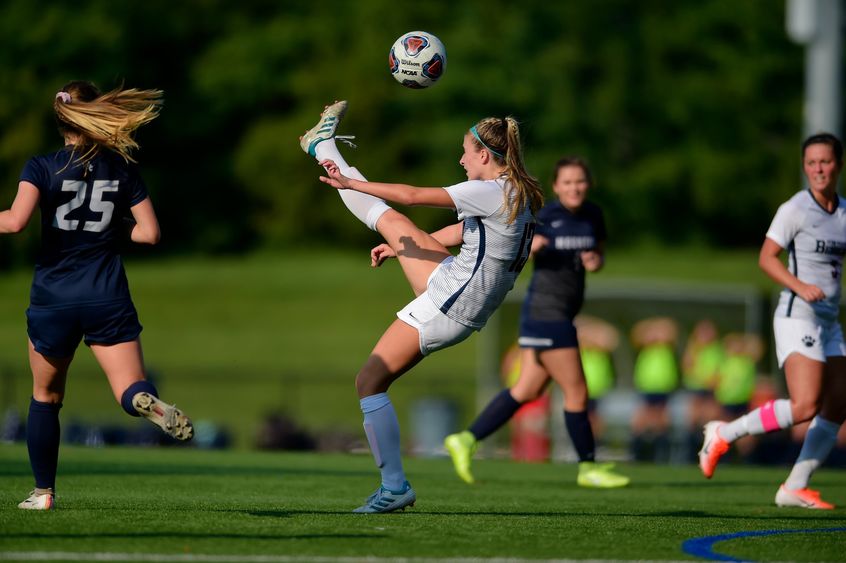 A Penn State Behrend soccer player kicks the ball above her head.