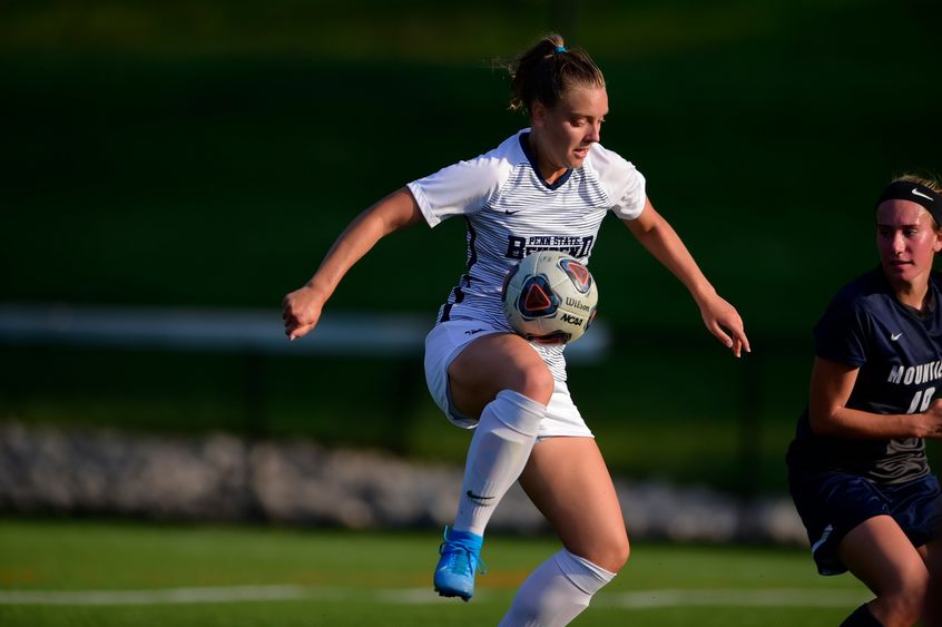 A female Penn State Behrend soccer player juggles the ball off her knee during a game.