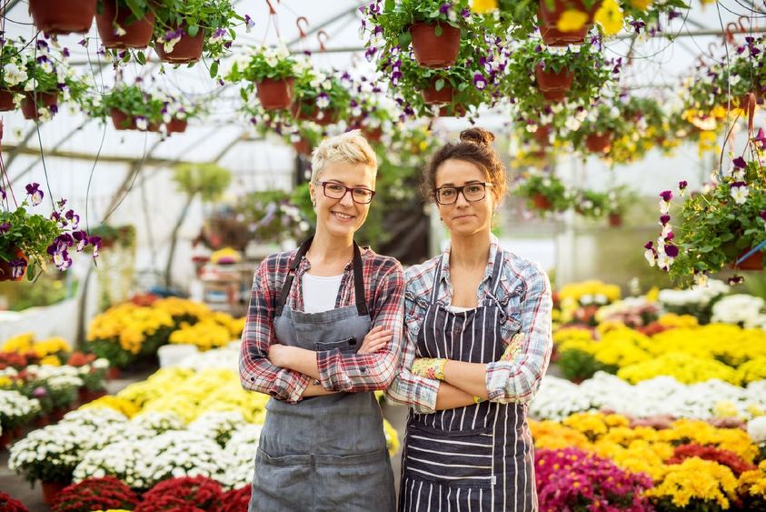 Two women pose in a floral-shop greenhouse