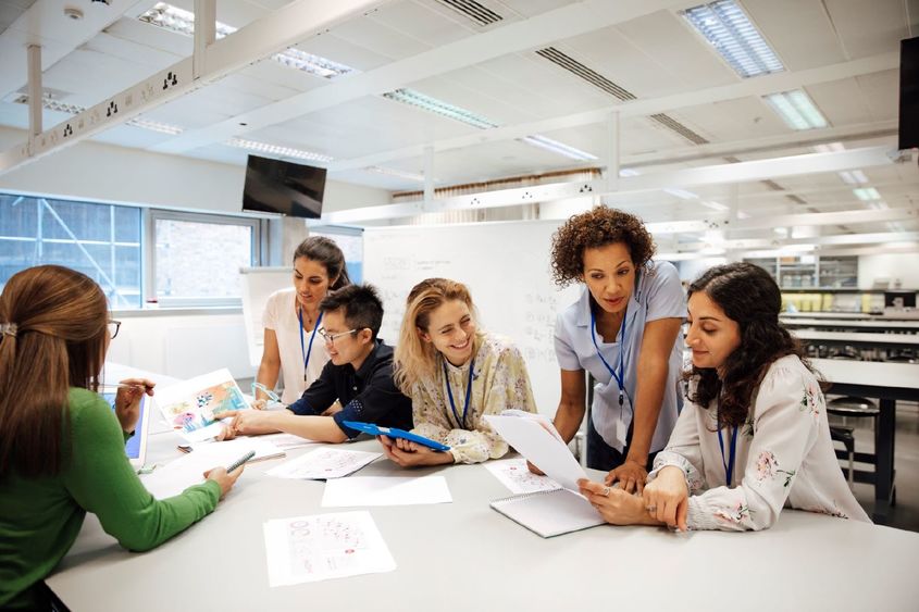 Adult students are gathered at a table working on an academic project together.