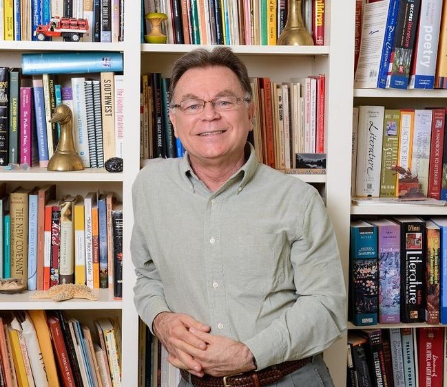 The poet Alberto Rios stands in front of a bookcase.