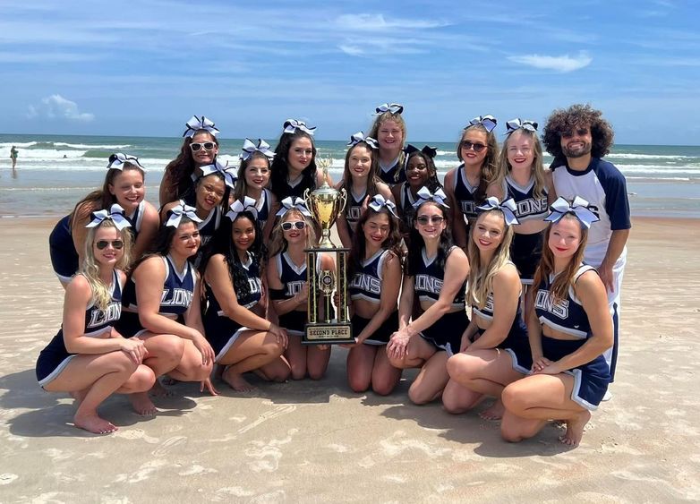 Penn State Behrend's competitive cheerleading team poses with a trophy on the beach in Florida.