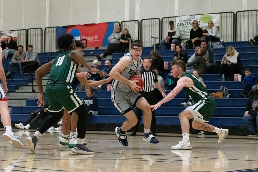 A Penn State Behrend basketball payer dribbles the ball between two defenders.