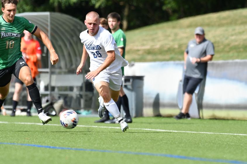 A Penn State Behrend men's soccer player advances the ball up the field.