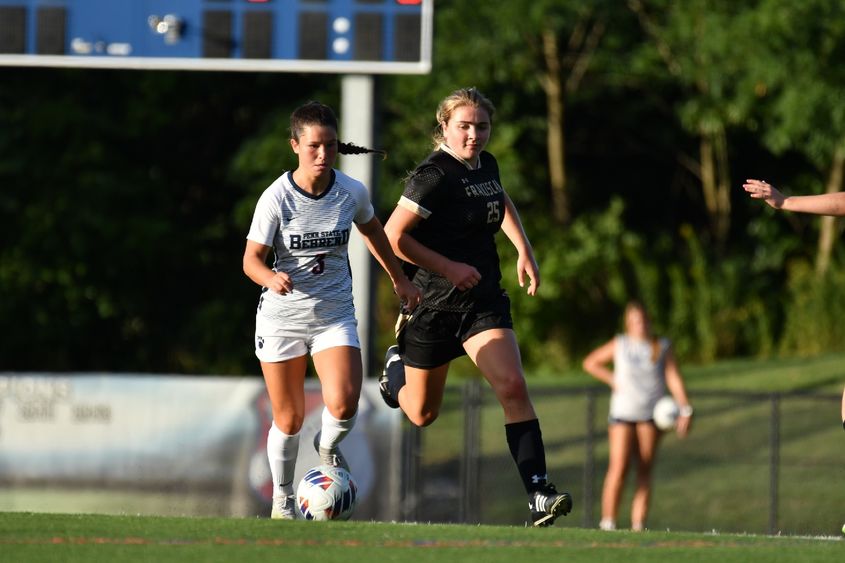 A Penn State Behrend soccer player advances the ball past her opponent.