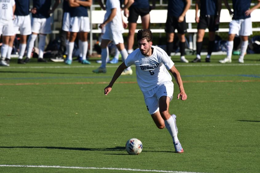 A Penn State Behrend men's soccer player advances the ball up midfield.