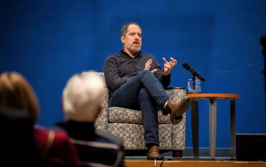 The actor Brendan Hunt gestures with his hands while sitting in a chair on stage at Penn State Behrend.