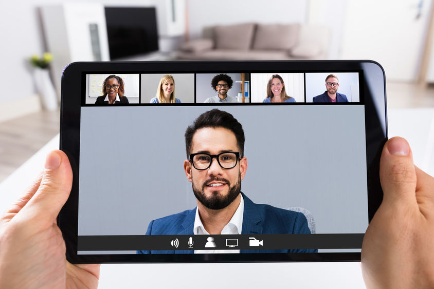 A person holds a tablet computer as it displays faces of Zoom-style meeting participants