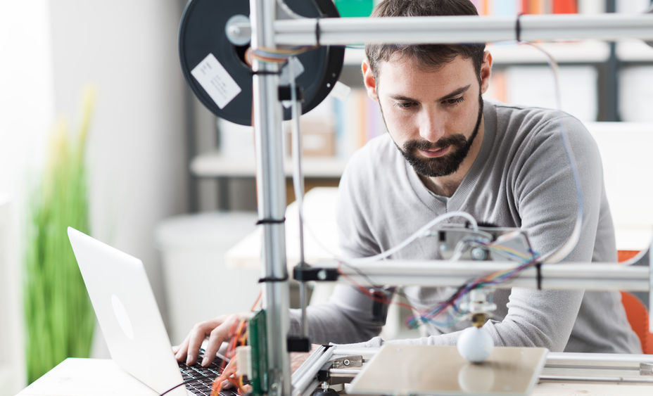 A bearded man works with a 3D printer