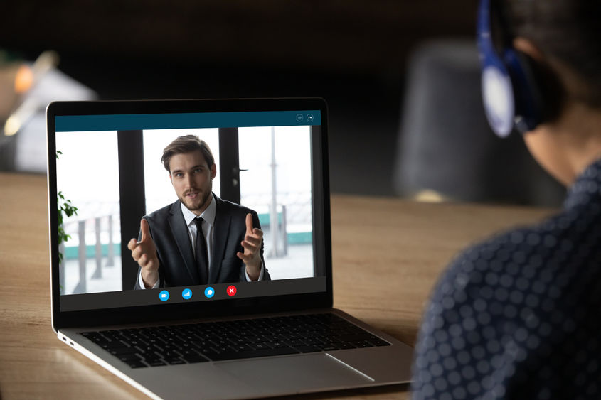 A man in a business suit talks to a woman through a computer video link.
