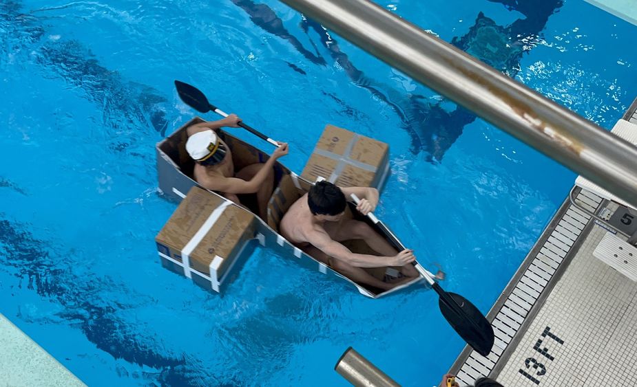 Two people paddle a cardboard boat in Penn State Behrend's pool.