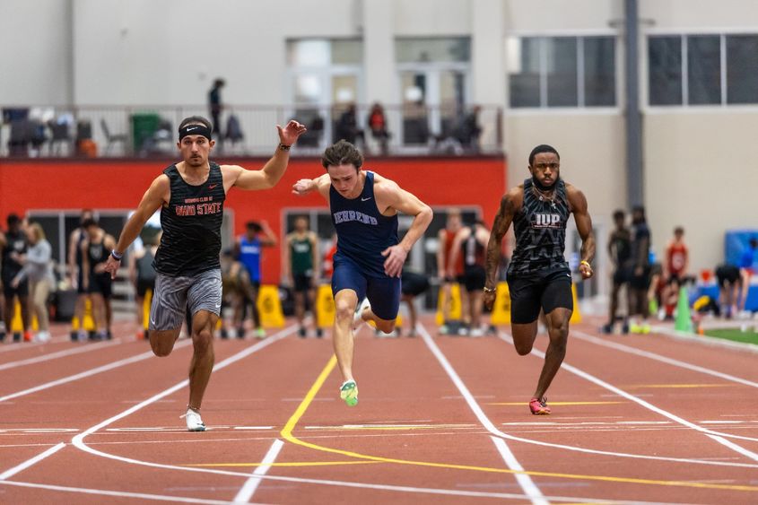 Three collegiate runners sprint to the finish line during a race.