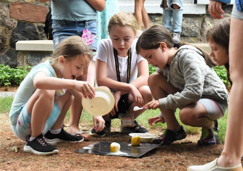 Three girls lean over a food-based science experiment outdoors at Penn State Behrend.