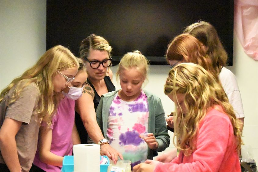A group of girls gather around a craft table as they make their own lip balms and body sprays.
