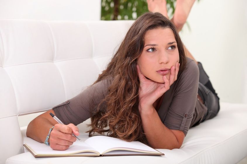 A woman looks to the side while writing in a journal.