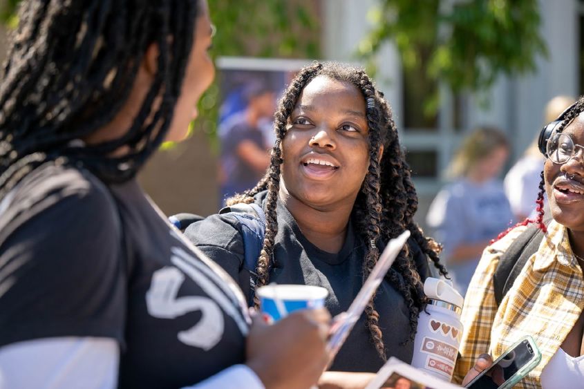 Three female students laugh while talking on the Reed Lawn during Penn State Behrend's Discovery Fair.