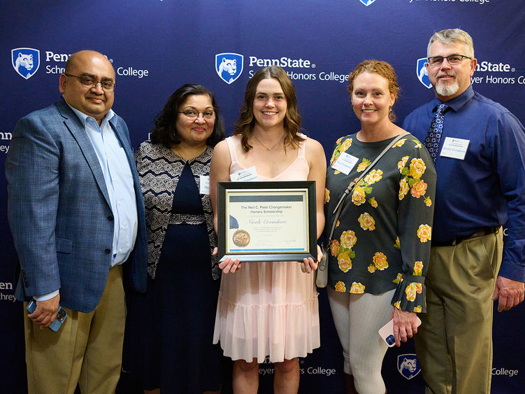 four people in front of a Schreyer banner, person in the center is holding a certificate