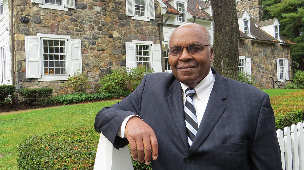 Retired Penn State Behrend faculty member Eva Tucker Jr. stands in front of Glenhill Farmhouse.