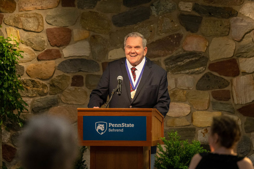 Former Gov. Tom Ridge smiles while standing at a podium at Penn State Behrend.