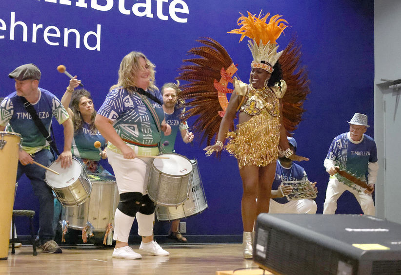 A costumed dancer jumps while on stage with several drummers.