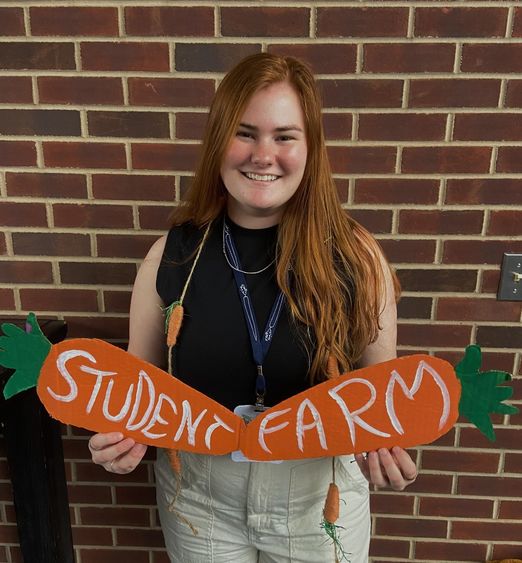 A person holds a sign that says Student Farm in front of a brick wall