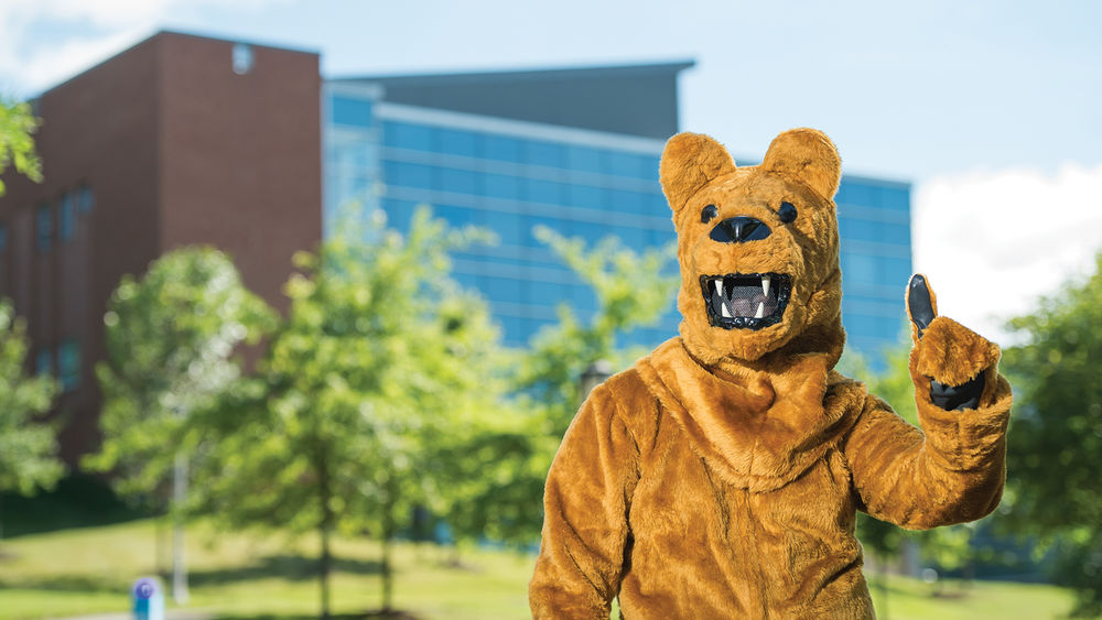 The Nittany Lion mascot poses in front of Burke Center at Penn State Behrend.