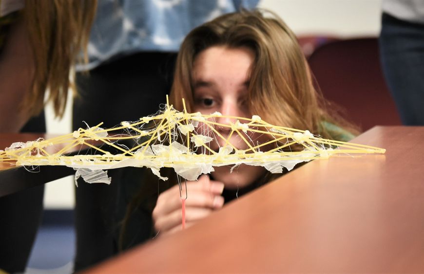 A female student looks closely at a bridge she built with spaghetti noodles.