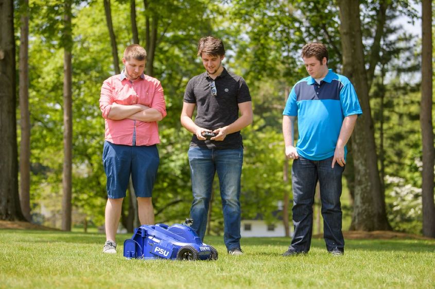 Three Penn State Behrend students test a remote-control lawn mower.