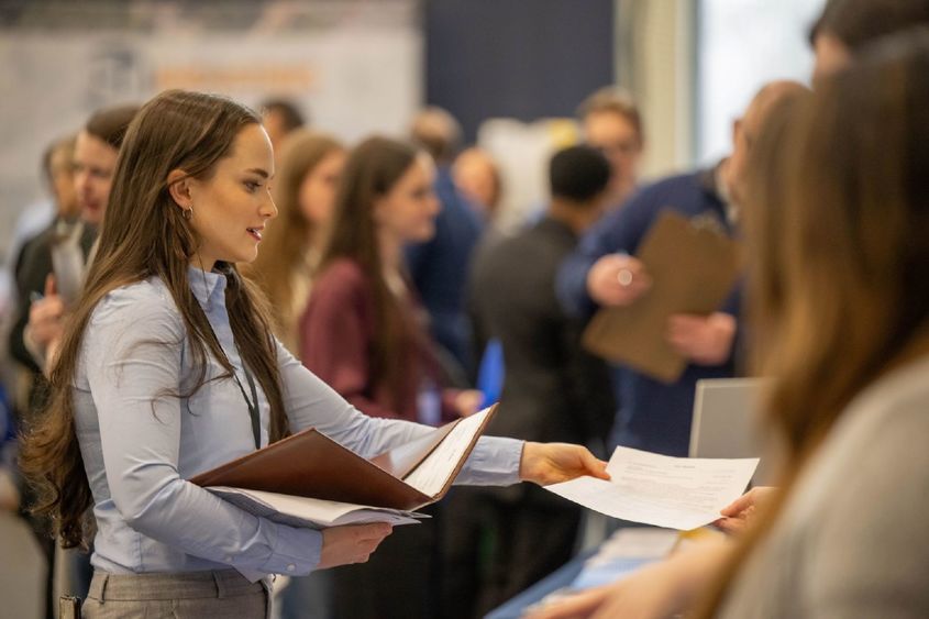A female student hands a resume to a recruiter at Penn State Behrend's career fair.
