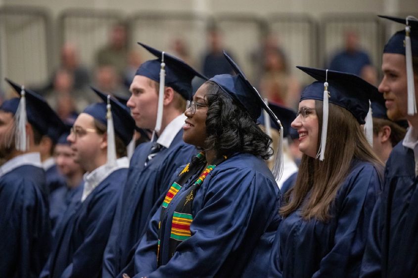 A row of graduates in caps and gowns listen to a speaker during Penn State Behrend's fall 2022 commencement program.