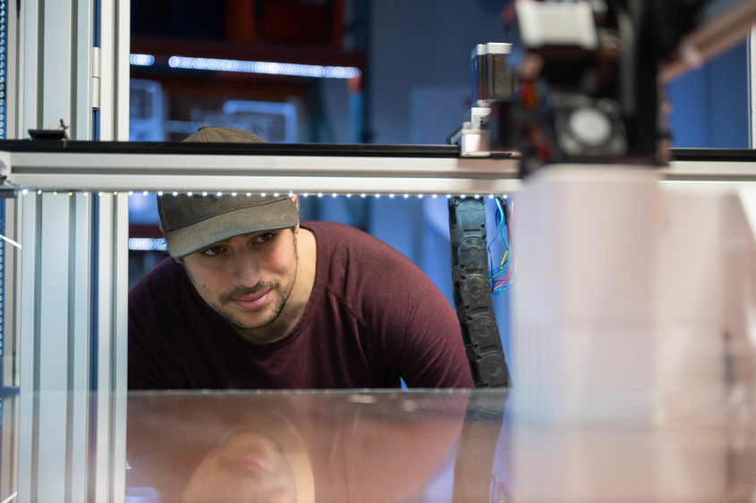 A Penn State Behrend student ducks down to look into a large-scale 3D printer.