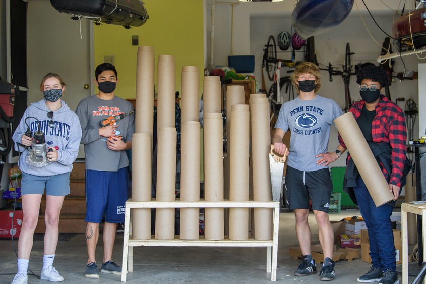 Four Penn State Behrend students pose next to a thongophone, a custom-built intstrument they constructed from used cardboard tubes.